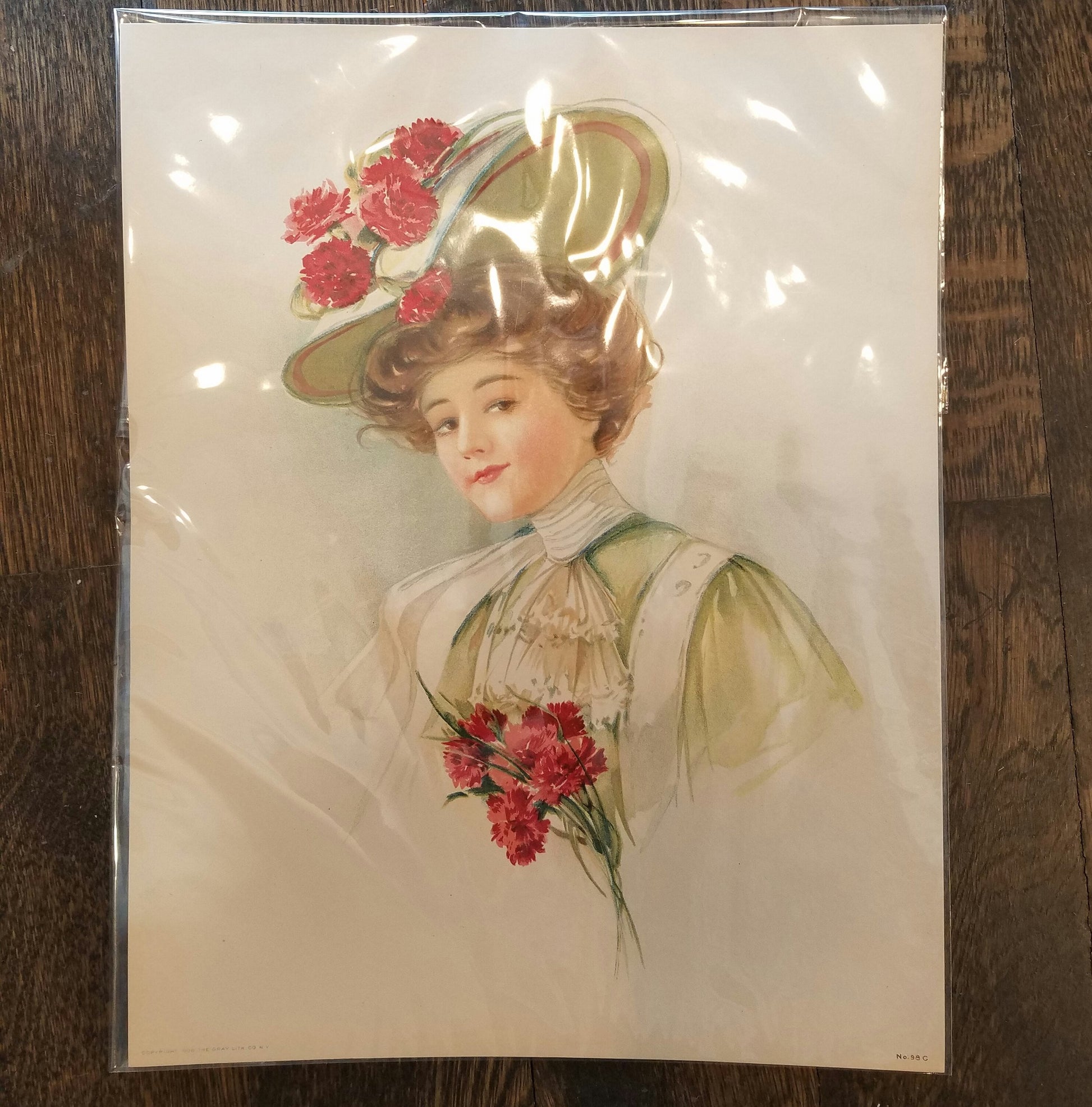 Victorian illustration of a brunette woman with brown eyes. Her hair is tied upward in a mint green, wide brimmed fancy hat with carnations on top of it. She has a high lace collar and ruffled lace bib of cream on her mint green dress. She is holding carnations.