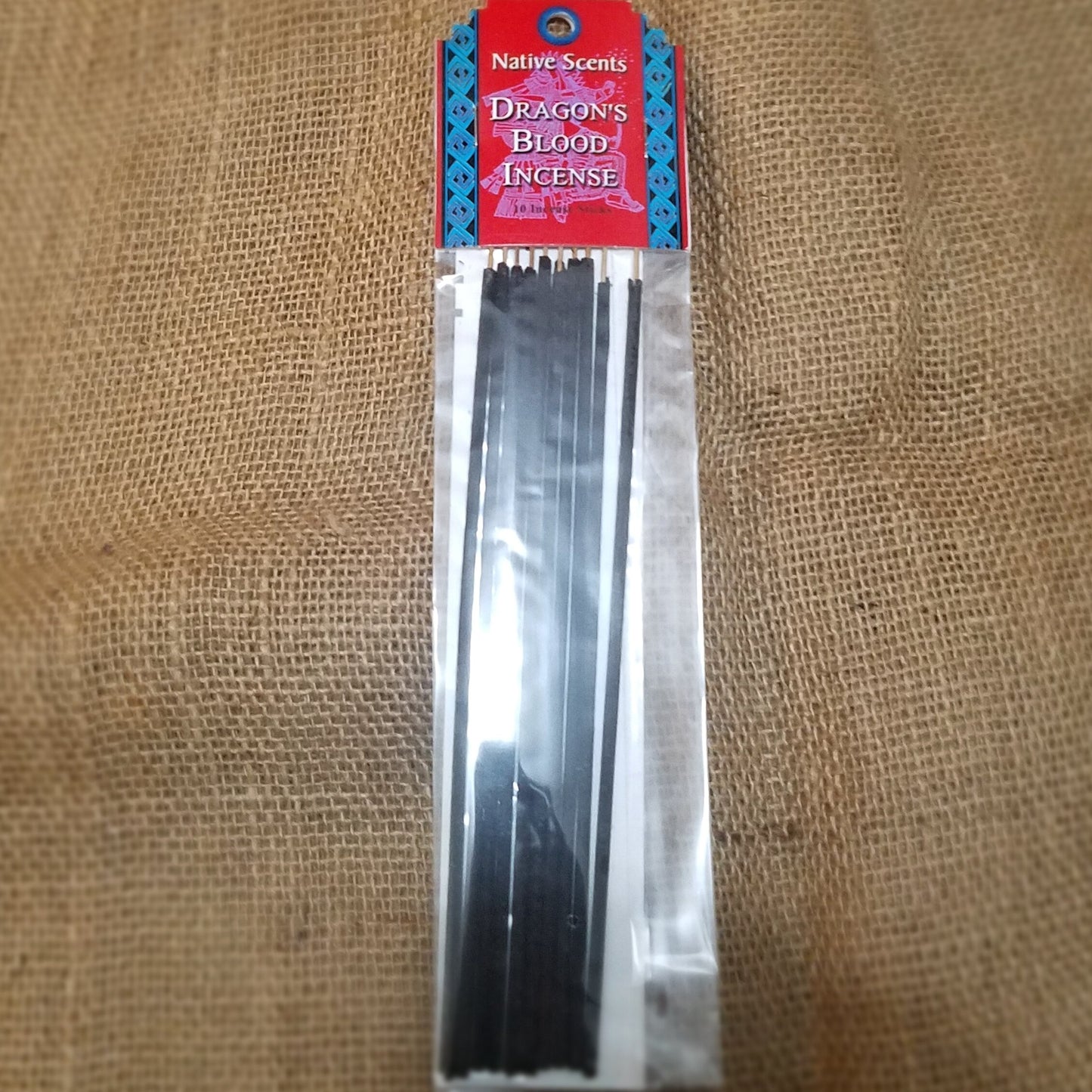 10 pack of dark incense sticks in clear celo packaging with red and blue cardboard label at top. Background is burlap.