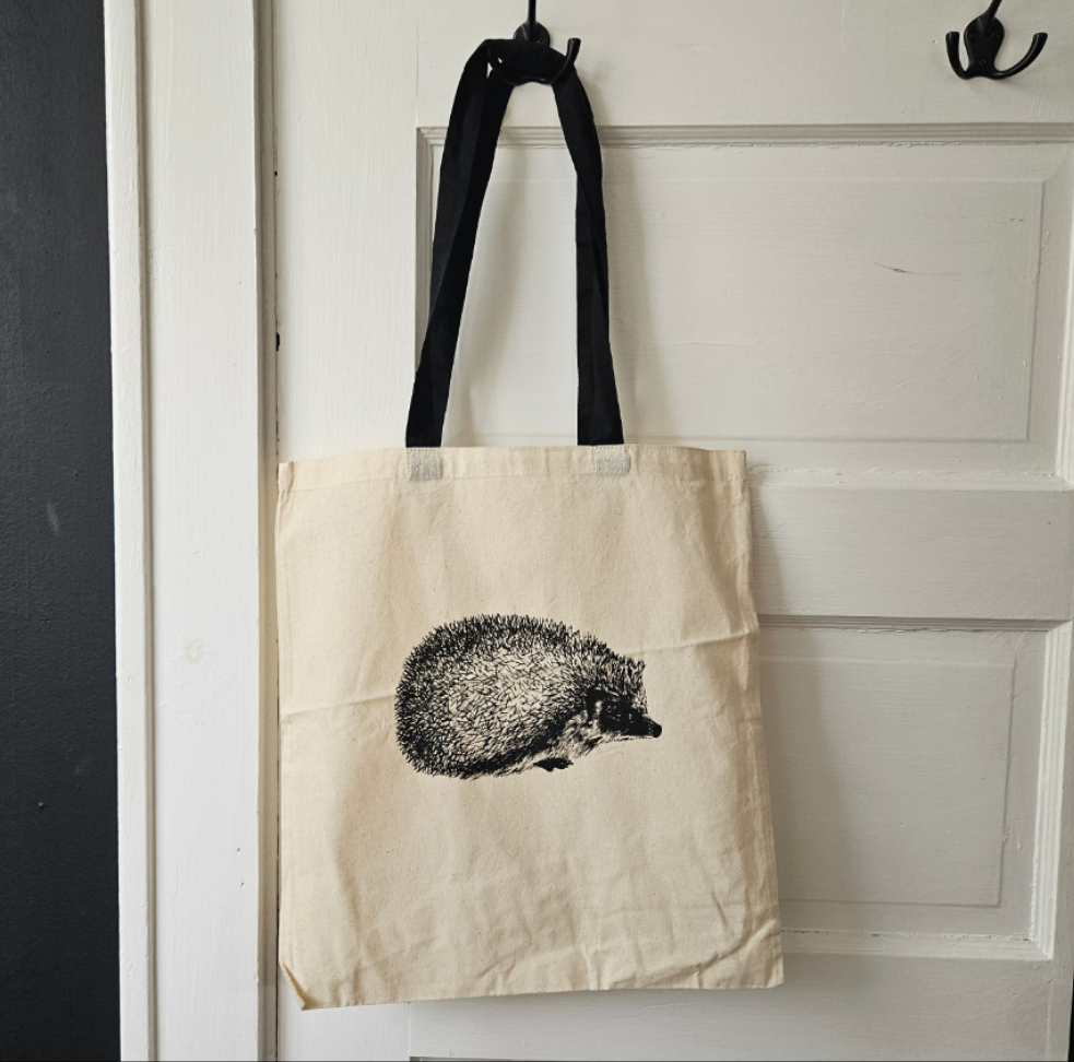 Black Sketch illustration of a Fruitbat hanging upside down from a branch, printed on a cream canvas totebag with a black handle.