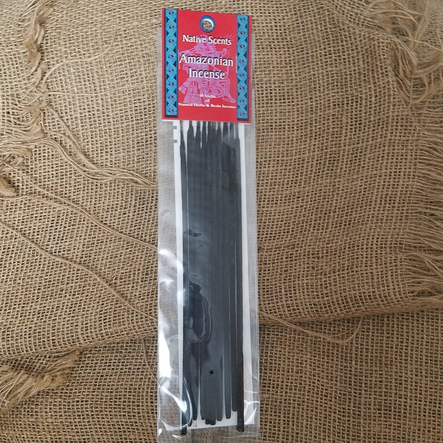 10 pack of dark incense sticks in celophane packaging with red and blue cardboard label at top. Background is burlap.