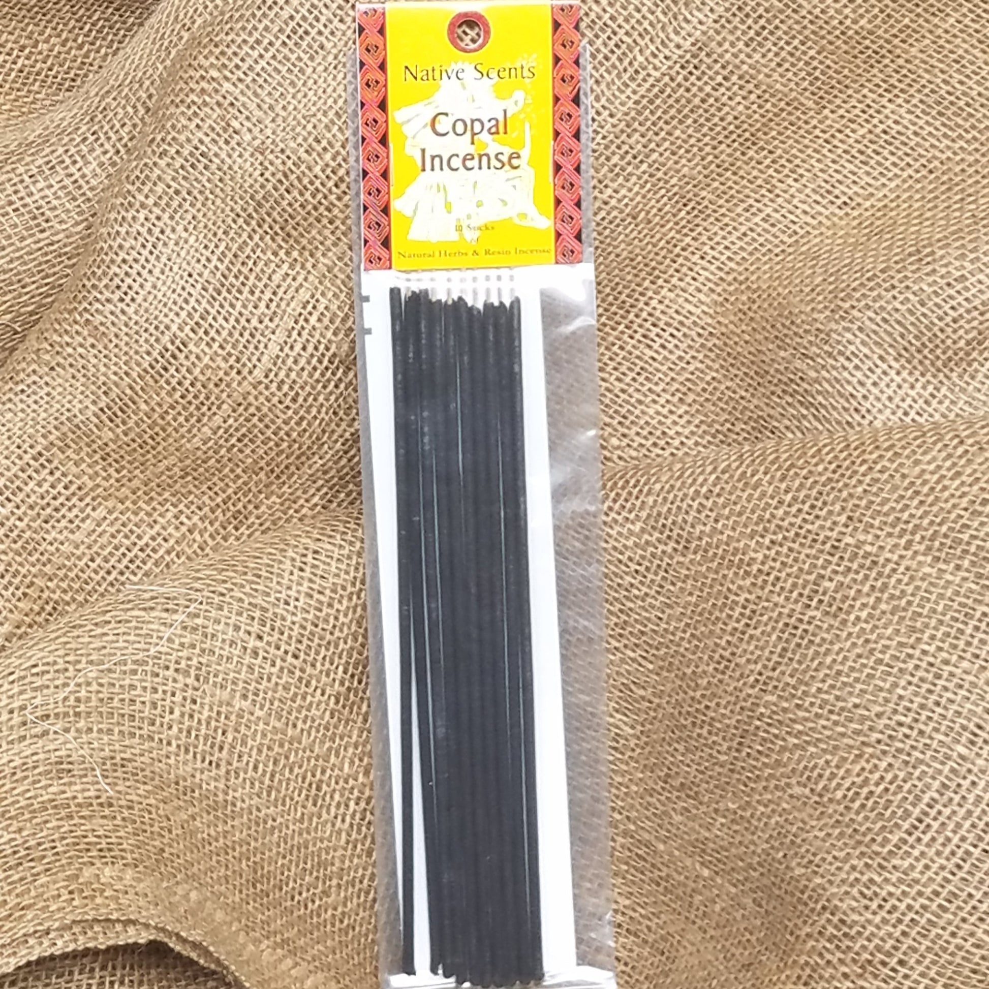 10 pack of dark copal incense in clear plastic package with saffron yellow and red and black label. Background is burlap cloth.