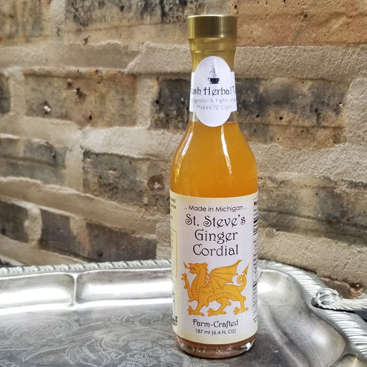 tall, thin, clear glass bottle of amber liquid. brick background. bottle sits on sterling silver antique serving tray.